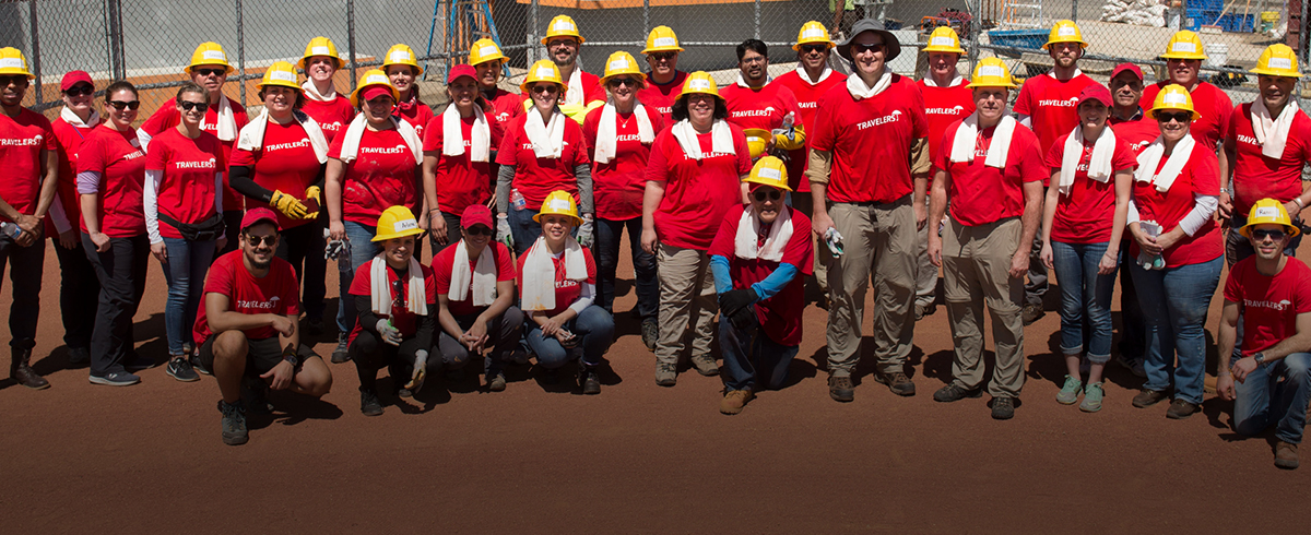 A group of people in red shirts and hard hats pose in front of a fenced area