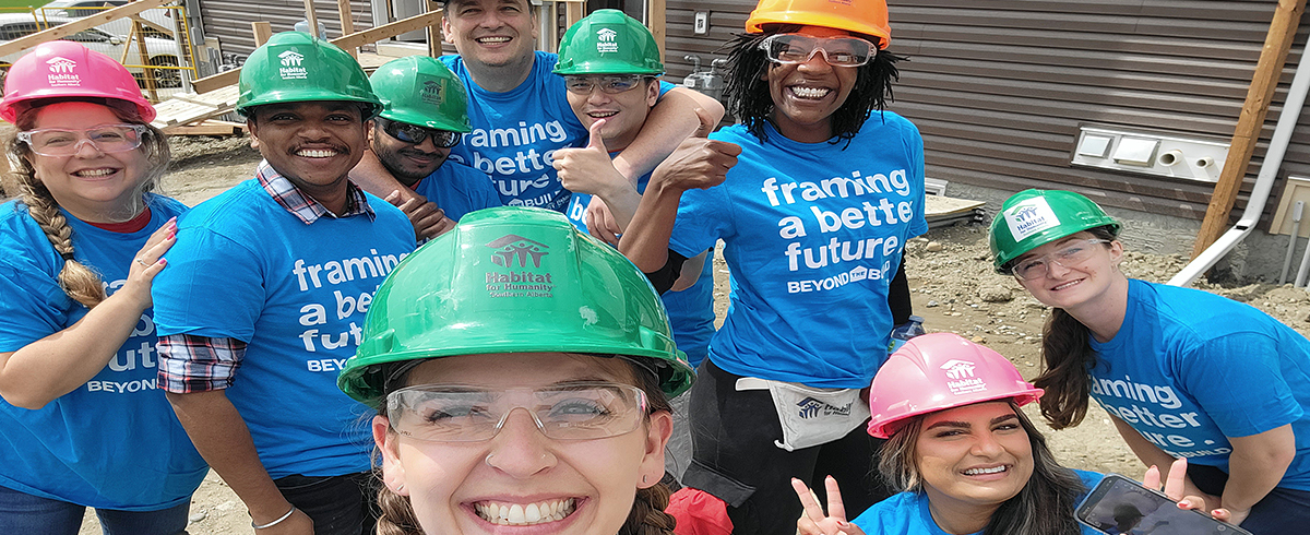 A group of people in blue shirts and hard hats pose outside